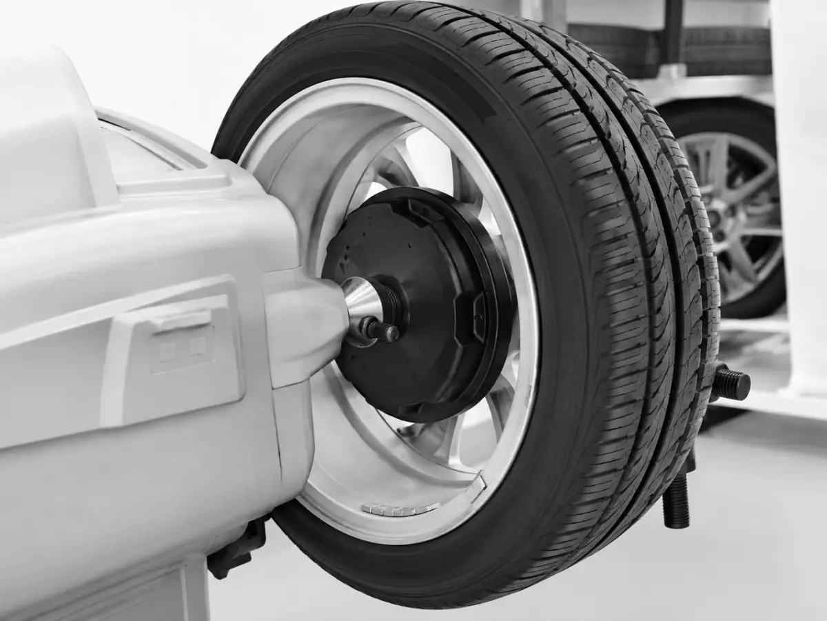 Mechaniker zieht auf der Montiermaschine einen Reifen auf eine Alufelge, daneben steht die Wuchtmaschine